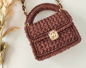 May include: A small brown crocheted handbag with a gold chain strap and a gold clasp. The bag has a textured surface and a slightly rounded shape.
