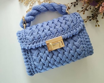 May include: A light blue crocheted handbag with a gold chain strap and a gold clasp. The bag has a woven texture and a rectangular shape.