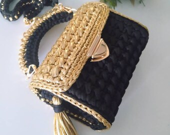 May include: A black and gold crocheted handbag with a gold chain strap and tassel. The bag has a flap closure with a gold clasp.