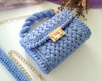 May include: A light blue crocheted handbag with a gold chain strap and a gold clasp. The bag has a braided rope handle.