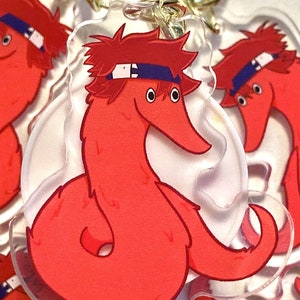 Può includere: Un verme rosso con una fascia rossa e occhi blu, che indossa una fascia blu con un disegno bianco. Il verme è arrotolato in un cerchio e ha uno sfondo bianco.