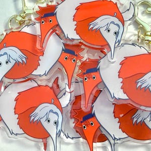 Può includere: Una collezione di portachiavi in acrilico trasparente con una creatura a forma di verme dei cartoni animati. Le creature hanno corpi arancioni, ali bianche e becchi lunghi. Ogni portachiavi ha una chiusura color oro.