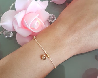 May include: A delicate white string bracelet with a small gold charm. The charm has a small diamond-like stone in the centre.