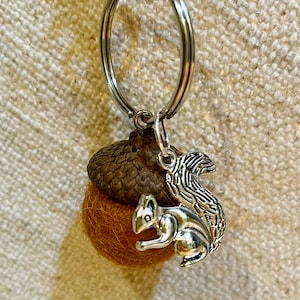 May include: A brown felt acorn keychain with a silver squirrel charm attached to a silver key ring.