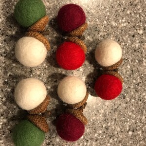 May include: Nine felt acorn ornaments in red, white, and green. The acorns are arranged in three rows of three.