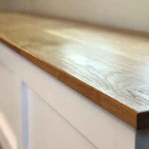 May include: Close-up of a light wood countertop with a white painted edge. The wood grain is visible and the surface is smooth.