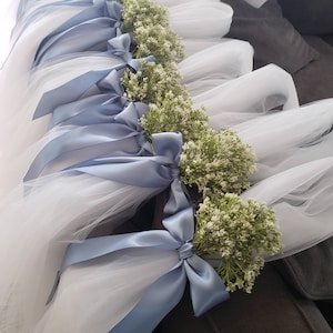 May include: White tulle fabric tied with light blue satin ribbons and small floral bouquets. The ribbons are tied into bows, and the flowers are small and white with green stems. The tulle is layered and appears soft.