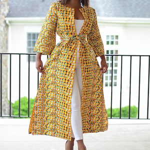 May include: A long yellow, blue, and red patterned kimono with a white belt tied at the waist. The kimono is worn over a white top and white pants. The person is wearing nude heels.