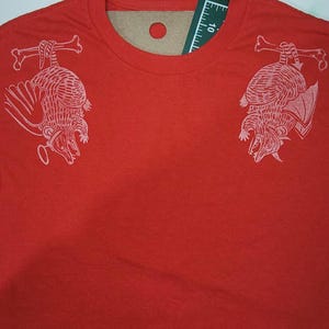 May include: Red t-shirt with a white graphic print of two armadillos hanging upside down from bones on each shoulder.