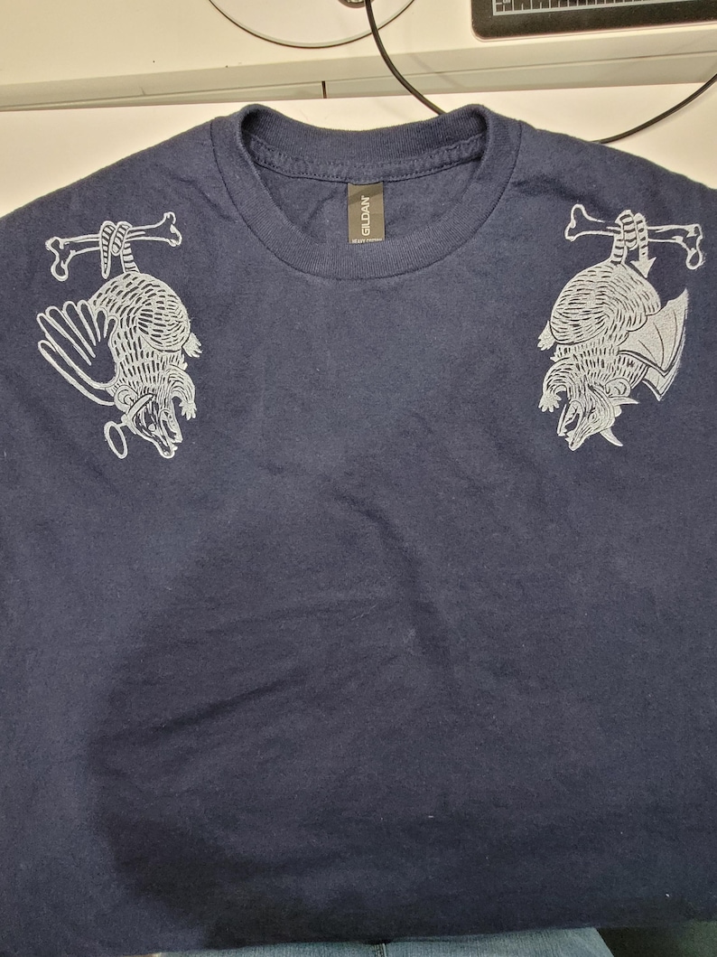 May include: A navy blue t-shirt with a white graphic print of two armadillos hanging from bones. The shirt has a Gildan brand tag.