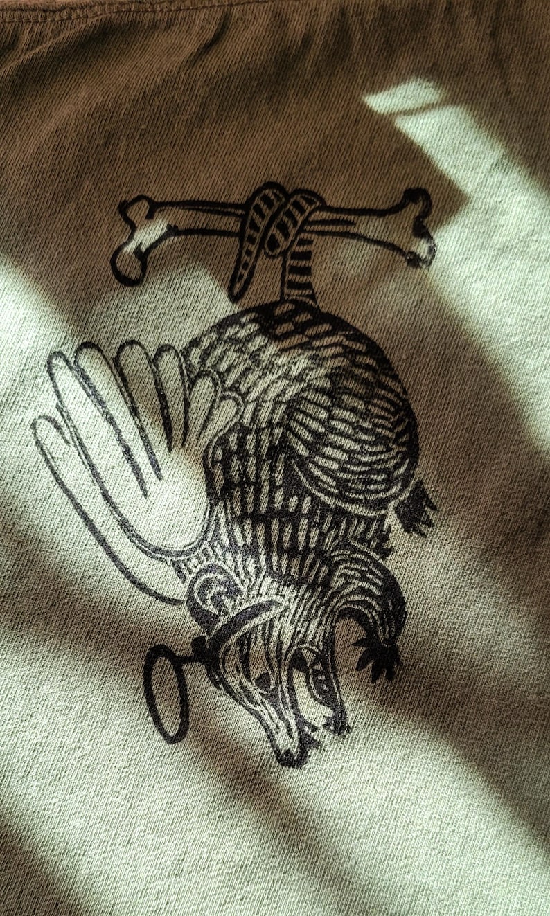 May include: A black and white graphic print of a rat with a bone tied around its neck. The rat is holding a key in its paw and is looking to the right. The graphic is on a light green fabric.