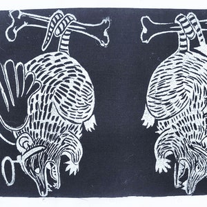 May include: Two black and white linocut prints of armadillos hanging upside down from bones. The armadillos have detailed markings and are in a menacing pose.