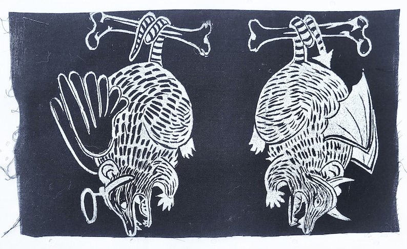 May include: Two black and white linocut prints of armadillos hanging upside down from bones. The armadillos have detailed markings and are in a menacing pose.