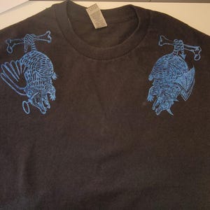 May include: Black t-shirt with a blue graphic print of two armadillos hanging from bones on each shoulder.