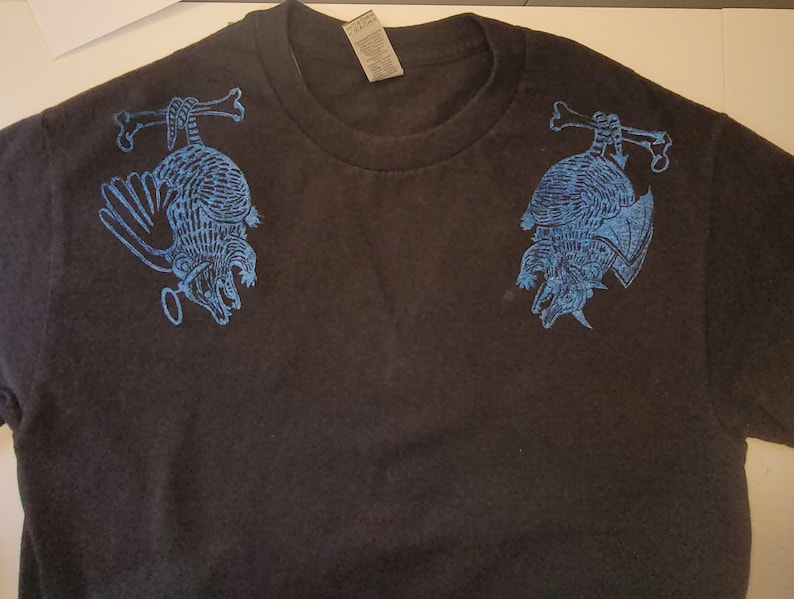 May include: Black t-shirt with a blue graphic print of two armadillos hanging from bones on each shoulder.