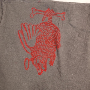 May include: A gray t-shirt with a red graphic of a possum hanging from two bones. The possum is drawn in a stylized, almost cartoon-like way.