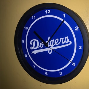 May include: A black and blue wall clock with white numbers and the word "Dodgers" in white on a blue background.