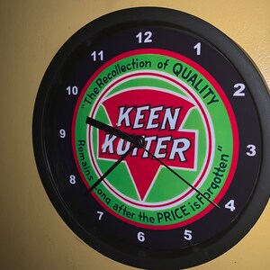 May include: A black wall clock with a white face and black hands. The clock has a green, red, and white logo in the center that says "Keen Kutter". The logo is surrounded by the text "The Recollection of QUALITY Remains Long After the PRICE is Forgotten".
