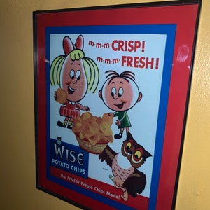 Könnte beinhalten: Eine gerahmte Vintage-Werbung für Wise Potato Chips mit einem Cartoon-Mädchen und -Jungen, die eine Schüssel mit Chips halten. Der Text lautet "m-m-m-CRISP! m-m-m-FRESH!" und "The FINEST Potato Chips Made!"