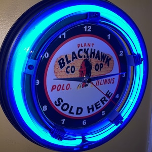 May include: A blue neon clock with a black face featuring the text "PLANT BLACKHAWK CO. OP POLO, ILLINOIS SOLD HERE".