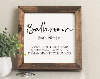 May include: A wooden framed sign with the word "Bathroom" written in cursive script. The sign defines the word as "a place of temporary quiet away from very demanding tiny humans."