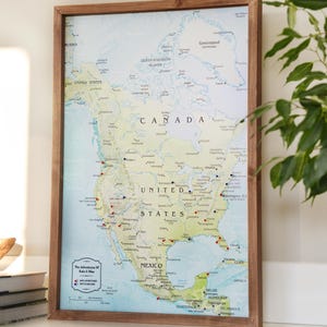 May include: A framed map of North America with a wooden frame. The map shows the United States, Canada, Mexico, and surrounding countries. The map is in a light blue and green color scheme with red dots marking cities. The text "The Adventures of Kate & Blue" is in a small rectangle in the lower left corner of the map.