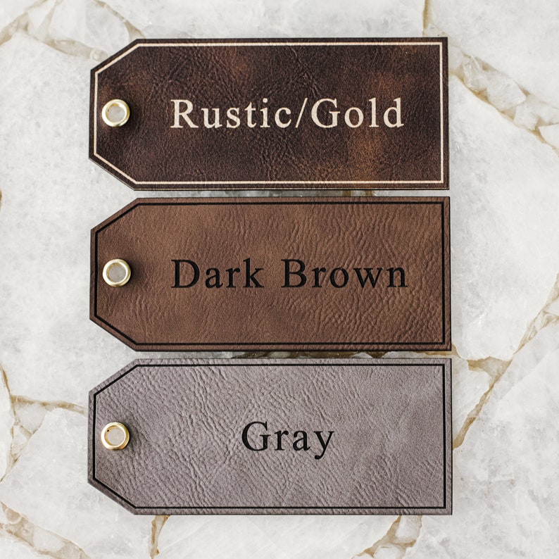 Op de afbeelding: Drie leren labels met verschillende kleuren en tekst. Het bovenste label is bruin met de tekst "Rustic/Gold". Het middelste label is donkerbruin met de tekst "Dark Brown". Het onderste label is grijs met de tekst "Gray".