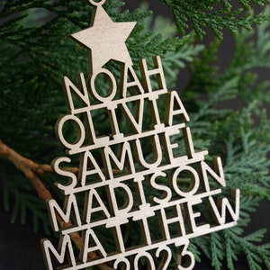 May include: A wooden Christmas tree bauble with the names Noah, Olivia, Samuel, Madison, Matthew, and the year 2023.