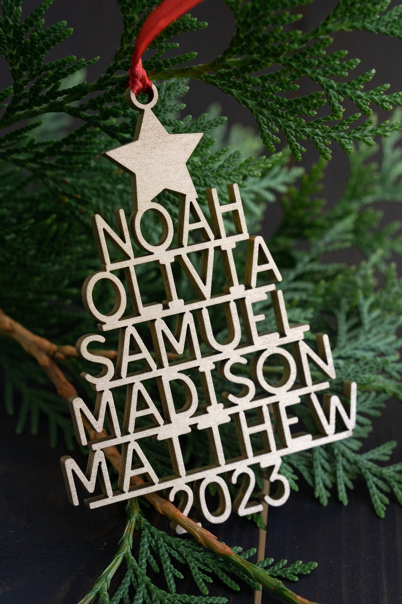 May include: A wooden Christmas tree bauble with the names Noah, Olivia, Samuel, Madison, Matthew, and the year 2023.