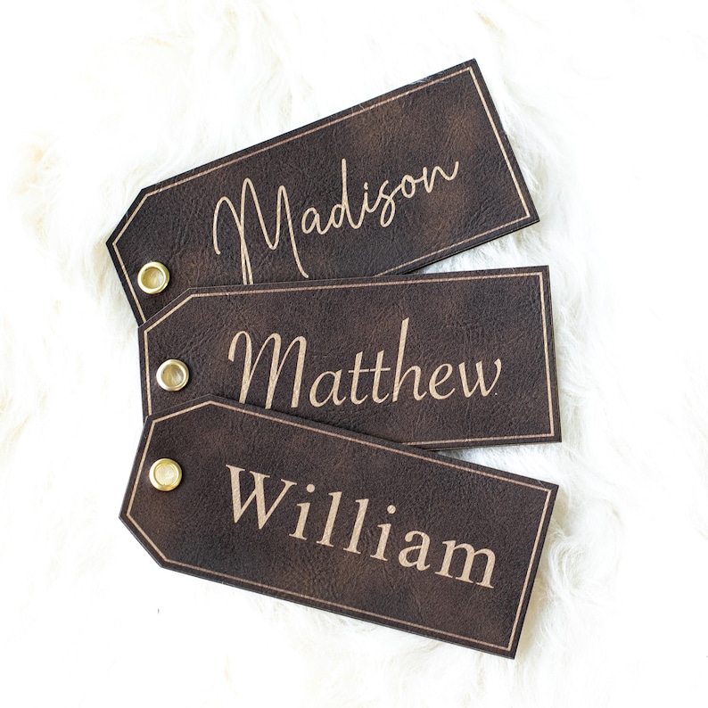 Op de afbeelding: Drie bruine leren cadeau-etiketten met gouden oogjes. De etiketten zijn op elkaar gestapeld. Het bovenste etiket zegt "Madison", het middelste etiket zegt "Matthew" en het onderste etiket zegt "William".