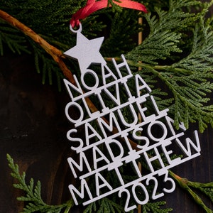 May include: A silver Christmas tree bauble with the names Noah, Olivia, Samuel, Madison, Matthew, and the year 2023.