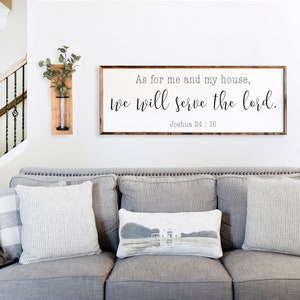 May include: A living room with a gray couch and two wooden wall vases with greenery. A framed sign above the couch reads "As for me and my house, we will serve the lord. Joshua 24:15."
