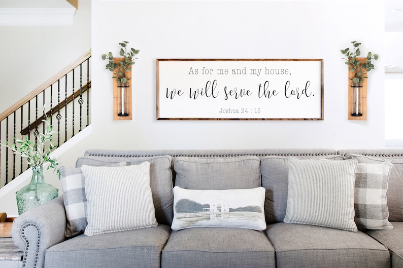 May include: A living room with a gray couch and two wooden wall vases with greenery. A framed sign above the couch reads "As for me and my house, we will serve the lord. Joshua 24:15."