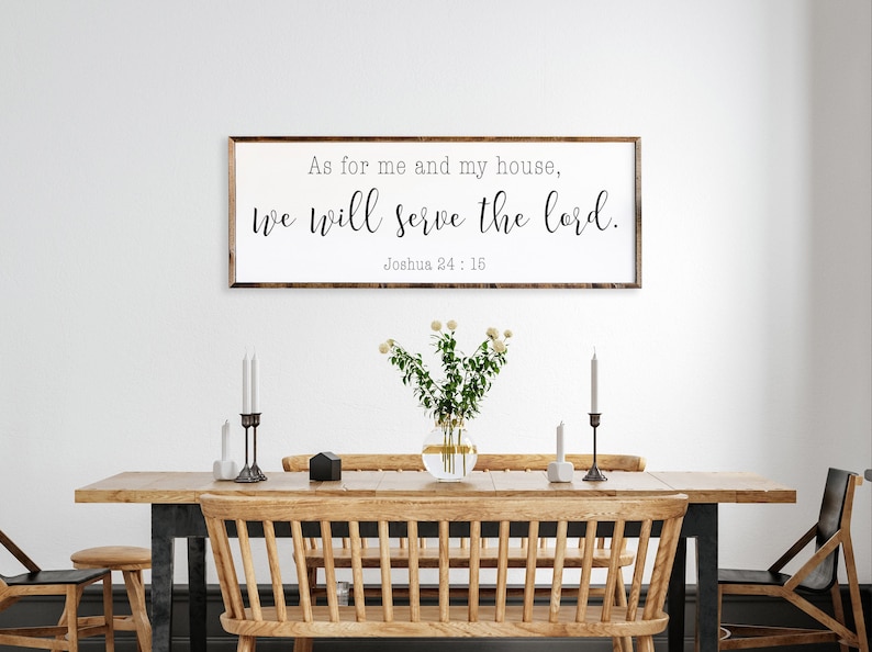 May include: A wooden sign with the text "As for me and my house, we will serve the lord. Joshua 24:15" hanging on a white wall above a wooden dining table with chairs.