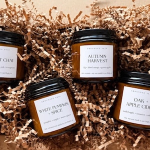 May include: Four amber glass jars with black lids, each featuring a white label with the brand name Grounded Skin and scent names: Forest Chai, Autumn Harvest, White Pumpkin + Spice, and Oak + Apple Cider, nestled in brown paper shred.