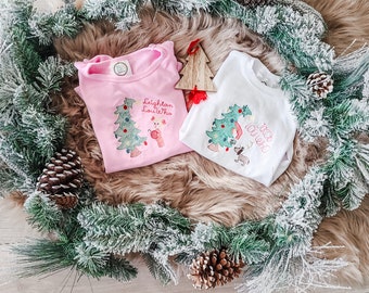 May include: A light pink long-sleeve shirt with an embroidered Christmas tree and a character, and a white long-sleeve shirt with an embroidered Christmas tree and a dog, featuring the text Leighton Lou Who and Jakob Lou Who respectively.