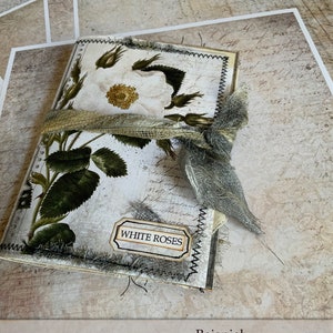 Peut inclure: Un journal fait main avec un motif de rose blanche et un ruban en toile de jute. La couverture est d&eacute;cor&eacute;e d'une &eacute;tiquette qui dit "Roses blanches".