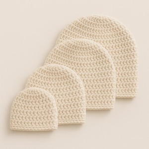 Op de afbeelding: Vier crèmekleurige, gehaakte mutsen van verschillende maten zijn diagonaal gerangschikt. De mutsen zijn gemaakt van een getextureerd garen en de haaksteek creëert een subtiel patroon. De hoeden zijn allemaal dezelfde kleur en stijl.