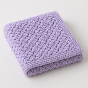 May include: A folded, square, lilac-coloured crocheted blanket. The blanket has a textured stitch pattern and a finished border. The soft, pastel colour and handmade appearance suggest a cosy, home decor item.