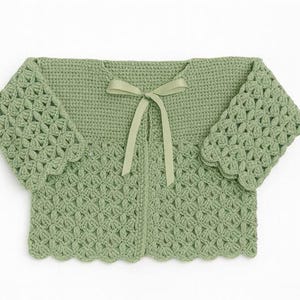 May include: A sage green crochet cardigan with a delicate floral pattern and scalloped edges. The short-sleeved top features a matching ribbon tie closure at the neckline. The handmade garment is displayed on a white background.