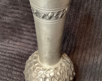 May include: A silver pewter vase with a textured, round base and a smooth, cylindrical neck. The neck is decorated with a band of embossed floral designs.