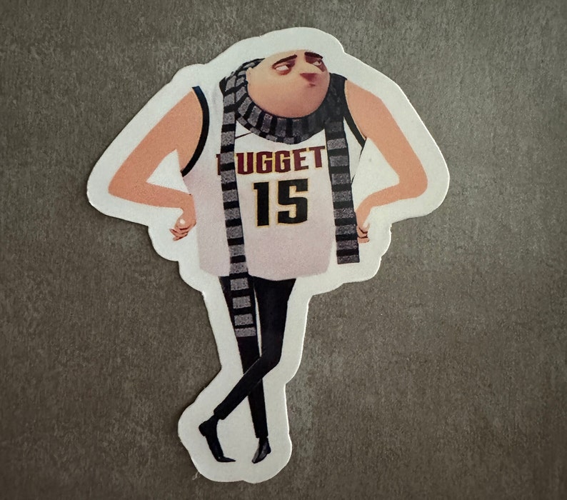 May include: A white and black sticker featuring a cartoon character wearing a white basketball jersey with the text "NUGGET 15" and a black and white striped scarf.