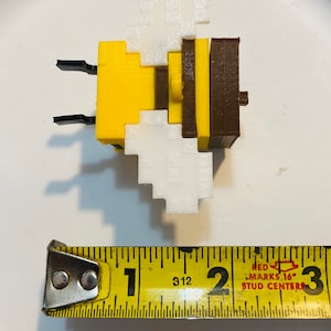 May include: A yellow and brown bee-shaped toy made of plastic blocks. The bee has white wings and is approximately 1 inch in size.