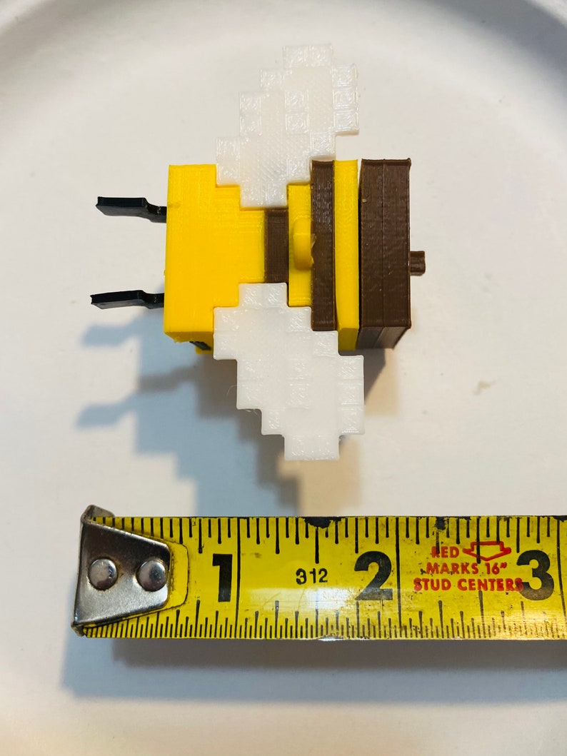 May include: A yellow and brown bee-shaped toy made of plastic blocks. The bee has white wings and is approximately 1 inch in size.