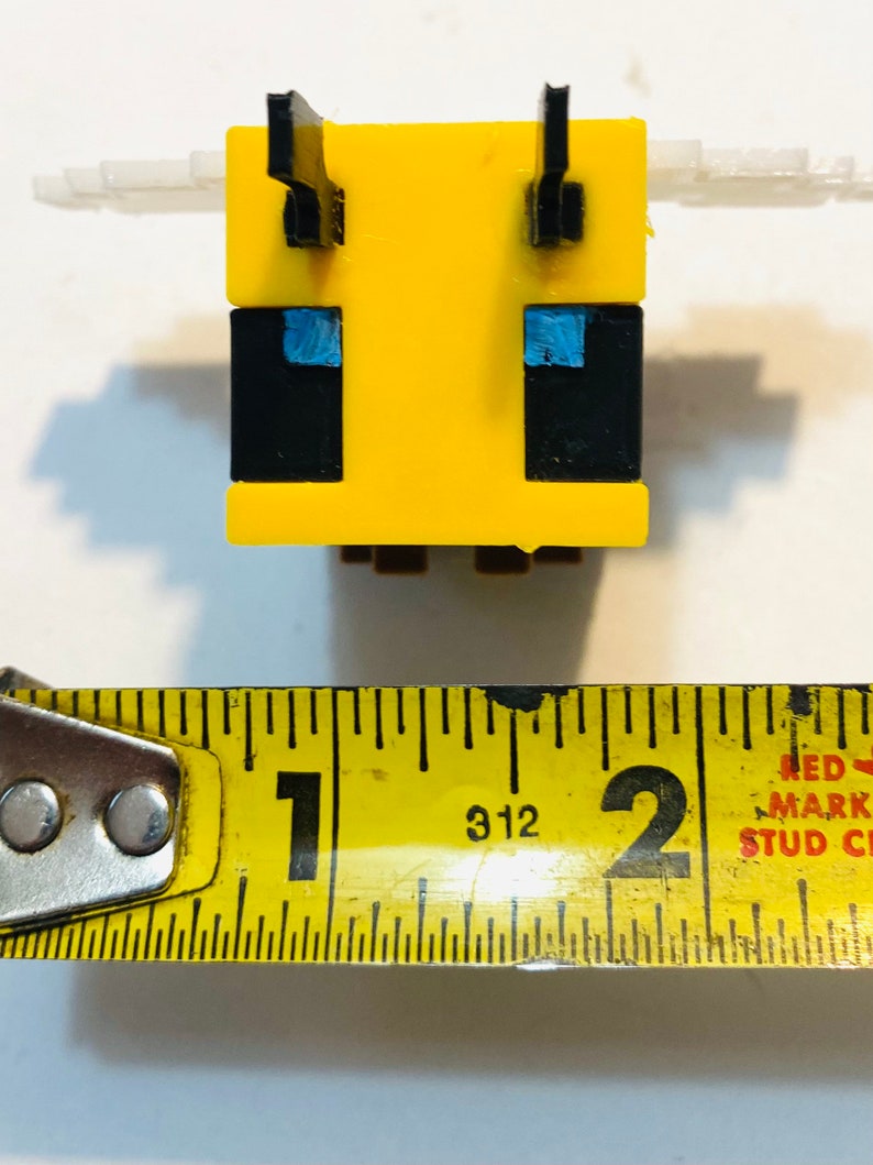 May include: A yellow and black bee-shaped Minecraft figure with blue eyes. The figure is about 1 inch tall.