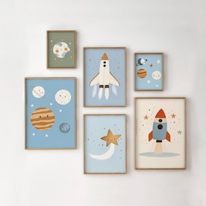 Puede incluir: Una colección de láminas enmarcadas con ilustraciones caprichosas de temática espacial. Las láminas muestran planetas, cohetes y estrellas en colores pastel suaves, incluyendo azul, naranja y verde. Cada lámina está enmarcada en dorado.