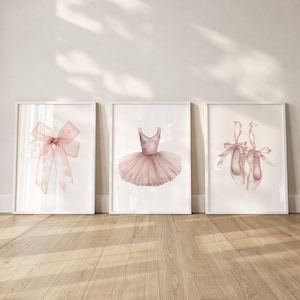 Puede incluir: Tres impresiones enmarcadas en acuarela con imágenes de temática de ballet. Las impresiones representan un lazo rosa, un tutú de ballet y un par de zapatillas de ballet con cintas. La obra de arte está sobre un fondo blanco y enmarcada en blanco.