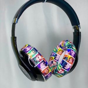 Puede incluir: Auriculares negros con un diseño colorido y estampado con una variedad de caras. Los auriculares tienen una diadema negra y auriculares con un diseño colorido y estampado con una variedad de caras.