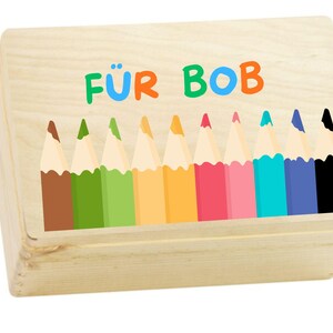 May include: A rectangular light-coloured wooden box featuring a printed graphic of ten coloured pencils in brown, green, lime, yellow, orange, red, pink, turquoise, blue, and black. The text FÜR BOB is printed in colourful letters above.