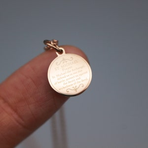 May include: A gold-toned pendant necklace with a round charm featuring an engraved prayer to Saint Michael the Archangel. The charm has a decorative border and the text reads "St. Michael the Archangel, defend us in our day of battle, protect us against the deceit and wickedness of the devil."